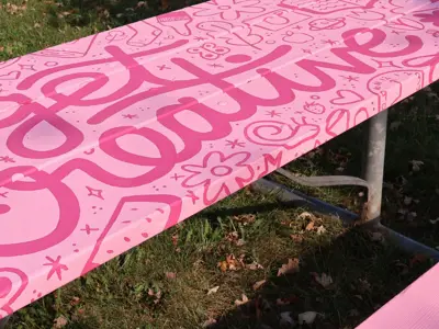 A picnic table painted bright pink with the words “get creative” and playful illustrations.